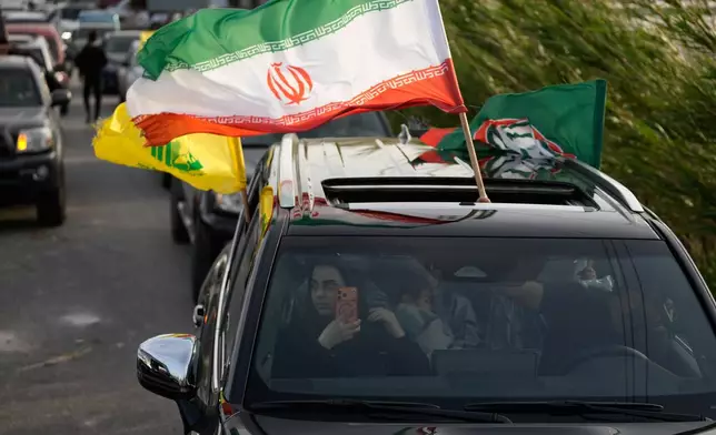 A displaced man waves the Iranian flag, as he returns with his family to their village following a ceasefire between Hezbollah and Israel, in Qasmiyeh near Tyre city, south Lebanon, Friday, April 17, 2026. (AP Photo/Mohammed Zaatari)