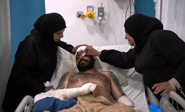 Mahmoud Sahmarani, 33, rests in a hospital bed as he is comforted by his mother and aunt after being injured in an Israeli airstrike, at Al-Najda Al-Shaabiya Hospital, in Nabatiyeh, southern Lebanon, Friday, April 17, 2026, following a ceasefire between Israel and Hezbollah. (AP Photo/Hassan Ammar)