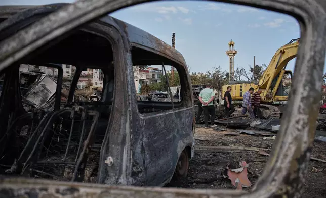 Locals residents walk among vehicles burned in an Israeli airstrike in Jibchit, southern Lebanon, Friday, April 17, 2026, following a ceasefire between Israel and Hezbollah. (AP Photo/Hassan Ammar)