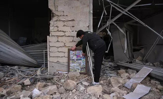 A Hezbollah health unit member Ali Fahos places portraits of his colleagues, killed during the previous war with Israel, next to a building destroyed in an Israeli airstrike in Jibchit, southern Lebanon, Friday, April 17, 2026, following a ceasefire between Israel and Hezbollah. (AP Photo/Hassan Ammar)