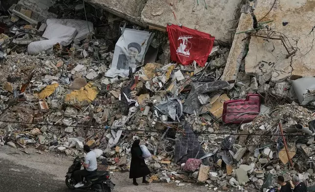 Residents pass the rubble of destroyed buildings, where a Hezbollah flag and an image of its late leader Hassan Nasrallah are placed, in Dahiyeh, Beirut's southern suburbs, Lebanon, Friday, April 17, 2026, following a ceasefire between Israel and Hezbollah. (AP Photo/Bilal Hussein)