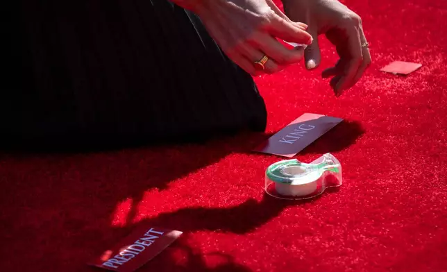 A staff member places tags for Britain's King Charles III and President Donald Trump on the red carpet before the arrival of the Britain's King Charles III and Queen Camilla at the White House, Monday, April 27, 2026, in Washington. (AP Photo/Mark Schiefelbein)