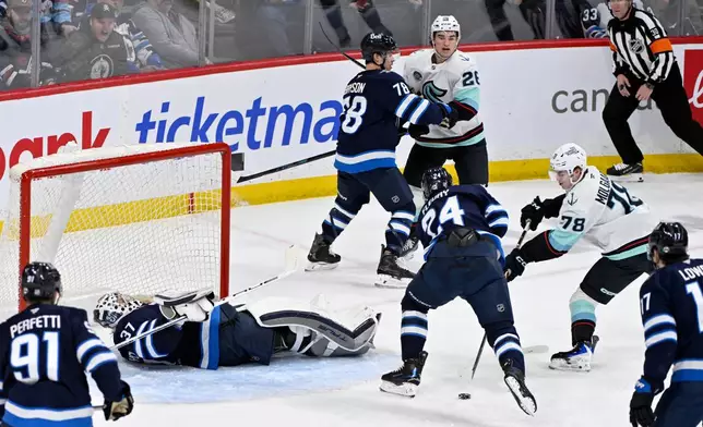 Seattle Kraken's Oscar Fisker Molgaard (78) tries to shoot against Winnipeg Jets goaltender Connor Hellebuyck (37) as Jets' Haydn Fleury (24) defends during second-period NHL hockey game action in Winnipeg, Manitoba, Monday, April 6, 2026. (Fred Greenslade/The Canadian Press via AP)