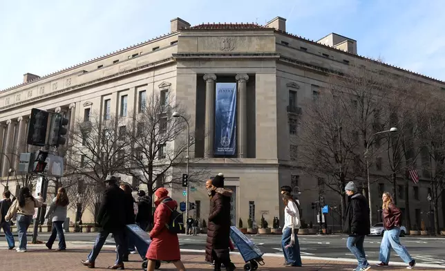FILE - Tourists walk past a banner with President Donald Trump hanging on the Department of Justice, Feb. 27, 2026, in Washington. (AP Photo/Rahmat Gul, File)