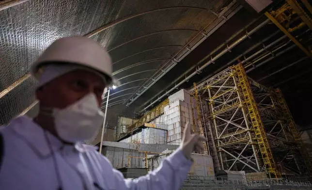 A technician of the Chernobyl nuclear power plant in Ukraine stands inside the New Safe Confinement structure and points toward the leaky, Soviet-built “sarcophagus” that covers the damaged reactor on April 6, 2026. (AP Photo/Evgeniy Maloletka)