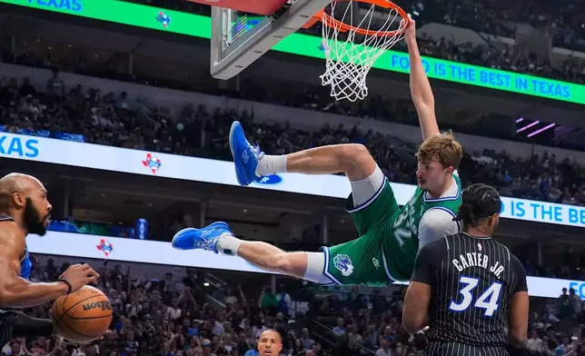 Dallas Mavericks forward Cooper Flagg (32) hangs on the rim after dunking over Orlando Magic's Wendell Carter Jr. (34) and Jevon Carter, left, in the first half of an NBA basketball game Friday, April 3, 2026, in Dallas. (AP Photo/Tony Gutierrez)