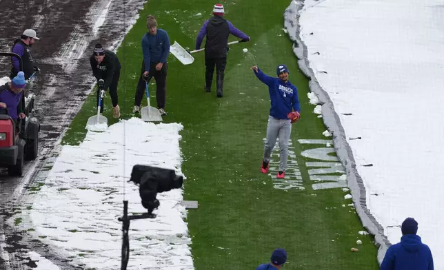 As the grounds crew works around him, Los Angeles Dodgers third baseman Santiago Espinal tosses a snowball at a coach while warming up to face the Colorado Rockies in a baseball game after a spring storm blanketed the intermountain West with a light covering of snow Friday, April 17, 2026, in Denver. (AP Photo/David Zalubowski)