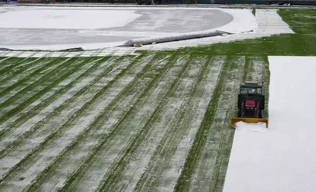 A grounds crew member clears snow from the outfield of Coors Field after a spring storm blanketed the intermountain West before the Colorado Rockies host the Los Angeles Dodgers Friday, April 17, 2026, in Denver. (AP Photo/David Zalubowski)