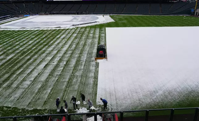 Grounds crew members toil to clear the outfield of Coors Field after a spring storm blanketed the intermountain West with a light covering of snow before the Colorado Rockies host the Los Angeles Dodgers in a baseball game Friday, April 17, 2026, in Denver. (AP Photo/David Zalubowski)