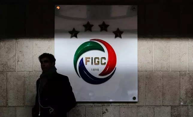 FILE - A journalist stands at the entrance of the FIGC Italian Soccer Federation, where a logo with four stars (one for each World Cup won) is seen partly in the shade, in Rome, on Nov. 14, 2017. (AP Photo/Alessandra Tarantino, File)