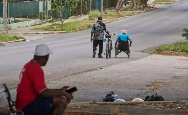 An elderly man makes his way in his wheelchair while a friend walks a bicycle beside him, in Havana, Cuba, Wednesday, April 15, 2026. (AP Photo/Ramon Espinosa)