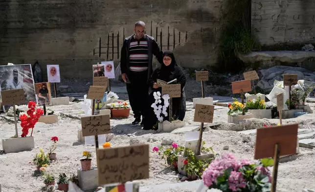 Zeinab Zeitoun, 50, right, and her husband Mohammed Farran, 60, whose six members of their family were killed in a an Israeli airstrike in Kfar Hatta village, visit their graves at a cemetery where civilians and Hezbollah fighters temporary buried in the southern port city of Sidon, Lebanon, Tuesday, April 14, 2026. (AP Photo/Mohammed Zaatari)