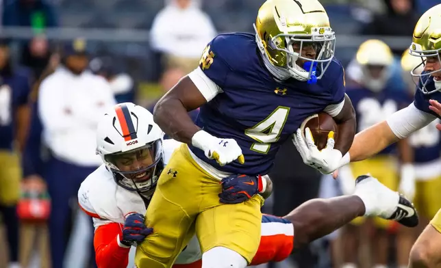 FILE - Notre Dame running back Jeremiyah Love (4) gets past a tackle-attempt by Virginia linebacker Kam Robinson, left, during the first half of an NCAA college football game Saturday, Nov. 16, 2024, in South Bend, Ind. (AP Photo/Michael Caterina, File)