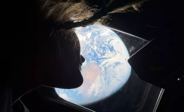 This image provided by NASA, astronaut and Artemis II mission specialist Christina Koch peers out of one of the Orion spacecraft's main cabin windows, looking back at Earth, as the crew travels towards the Moon on Thursday, April 2, 2026. (NASA via AP)