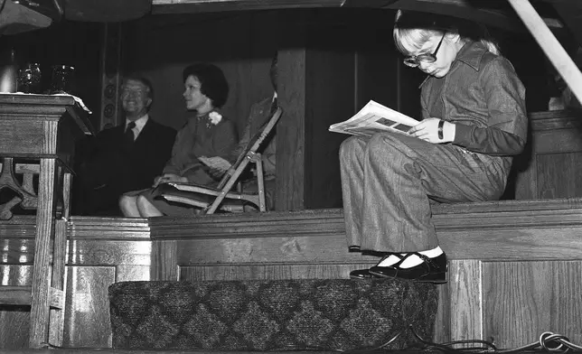 FILE - Amy Carter catches up on her reading as she waits with her parents, Jimmy and Rosalynn Carter, for the Democratic presidential candidate to address a rally at the Tabernacle Baptist Church on Chicago's South Side, Oct. 10, 1976. (AP Photo/Jack Thornell, File)