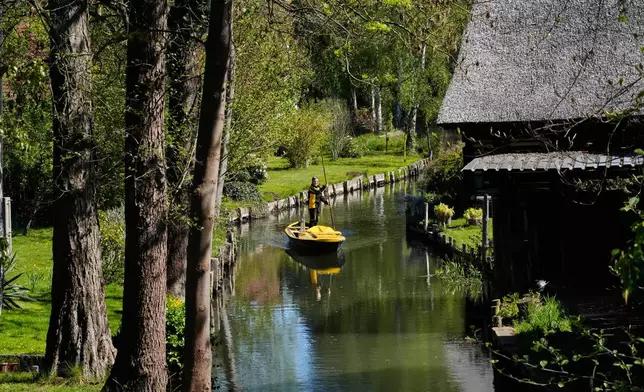 Mailwoman Andrea Bunar stands on a boat, using one long oar to row, steer, and navigate the barge through narrow waterways during the first tour of the summer when mail delivered on the waterways in the village Lehde in Luebbenau, Germany, Wednesday, April 29, 2026. (AP Photo/Markus Schreiber)
