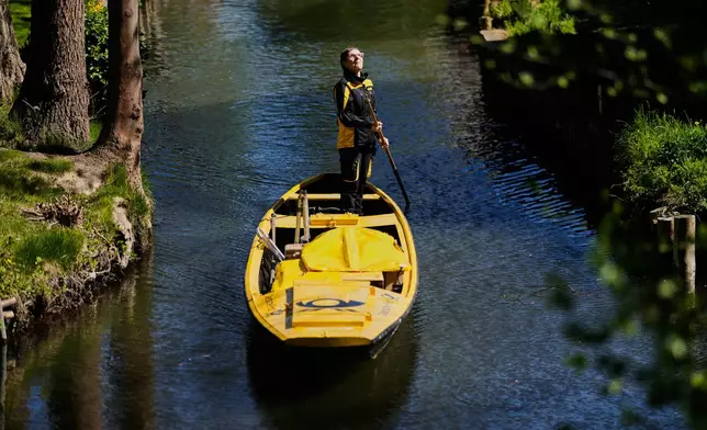 Mailwoman Andrea Bunar stands on a boat, using one long oar to row, steer, and navigate the barge through narrow waterways during the first tour of the summer when mail delivered on the waterways in the village Lehde in Luebbenau, Germany, Wednesday, April 29, 2026. (AP Photo/Markus Schreiber)