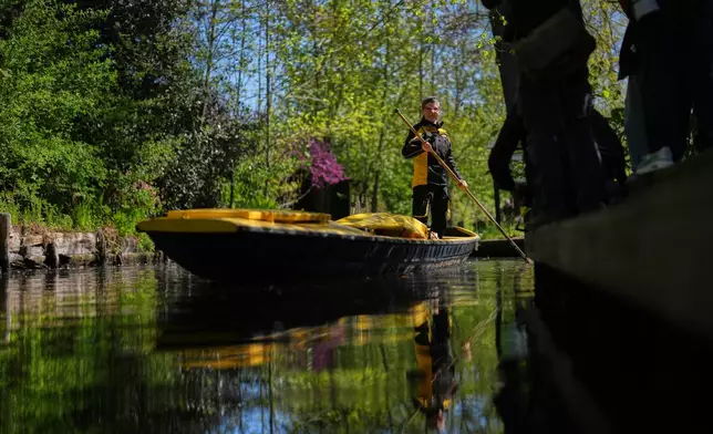 Mailwoman Andrea Bunar stands on a boat, using one long oar to row, steer, and navigate the barge through narrow waterways during the first tour of the summer when mail delivered on the waterways in the village Lehde in Luebbenau, Germany, Wednesday, April 29, 2026. (AP Photo/Markus Schreiber)