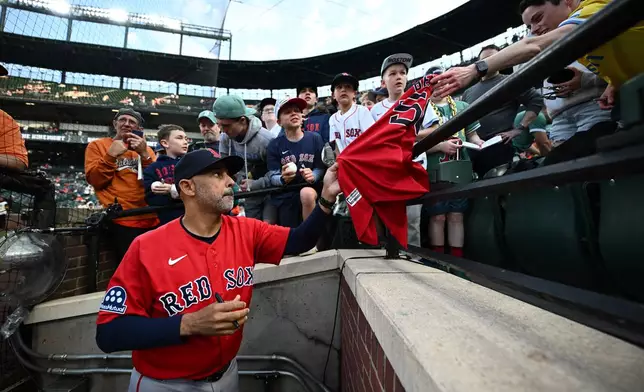 Boston Red Sox manager Alex Cora, foreground, gives autographs to fans before a baseball game against the Baltimore Orioles, Friday, April 24, 2026, in Baltimore. (AP Photo/Nick Wass)