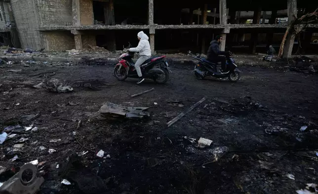 Two men ride scooters past charred debris at the site of an Israeli strike in Beirut, Lebanon, Wednesday, April 1, 2026. (AP Photo/Hassan Ammar)