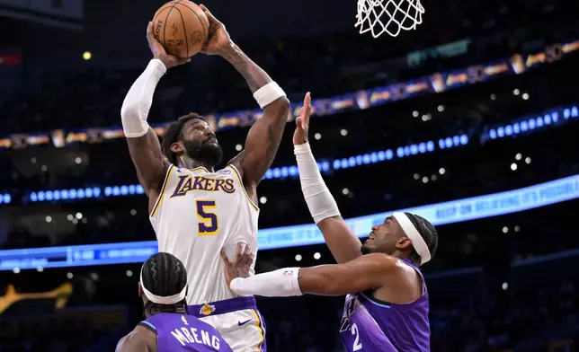 Los Angeles Lakers center Deandre Ayton (5) goes up to dunk as he is defended by Utah Jaz guard Bez Mbeng, bottom left, and forward Blake Hinson, right, during the first half of an NBA basketball game Sunday, April 12, 2026, in Los Angeles. (AP Photo/Jayne Kamin-Oncea)