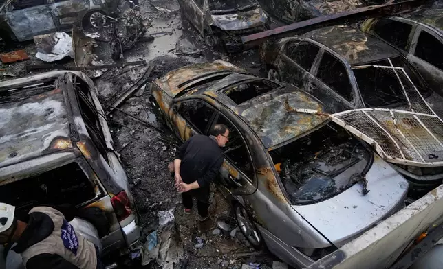 A man peers inside a burned car at the site of an Israeli airstrike that struck a building in Beirut, Lebanon, Wednesday, April 8, 2026. (AP Photo/Hassan Ammar)
