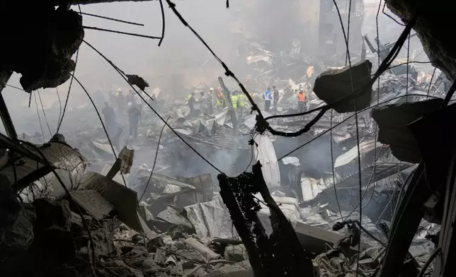 Firefighters, volunteers and first responders walk on smoldering debris at the site of an Israeli airstrike that struck a building in Beirut, Lebanon, Wednesday, April 8, 2026. (AP Photo/Hassan Ammar)