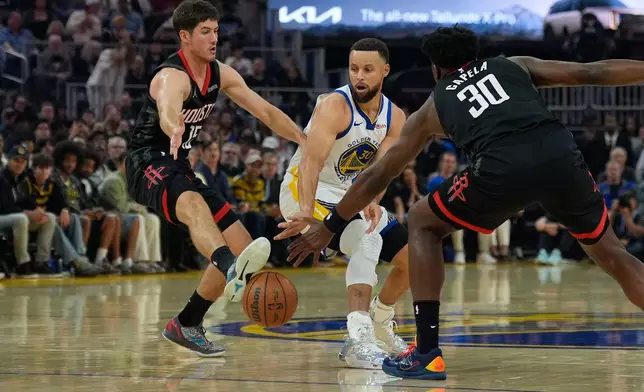 Houston Rockets guard Reed Sheppard, left, kicks a pass by Golden State Warriors guard Stephen Curry, center, during the first half of an NBA basketball game, Sunday, April 5, 2026, in San Francisco. (AP Photo/Godofredo A. Vásquez)
