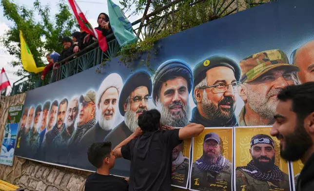 Hezbollah supporters hang portraits of Hezbollah fighters killed in Israeli airstrikes during their funeral procession in the southern village of Kfar Sir, Lebanon, Tuesday, April 21, 2026. (AP Photo/Hassan Ammar)