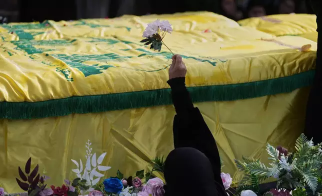 A woman places flowers on coffins of Hezbollah fighters who were killed before the ceasefire in the war between Hezbollah and Israel, during a mass funeral procession in the southern village of Kfar Sir, Lebanon, Tuesday, April 21, 2026. (AP Photo/Hassan Ammar)