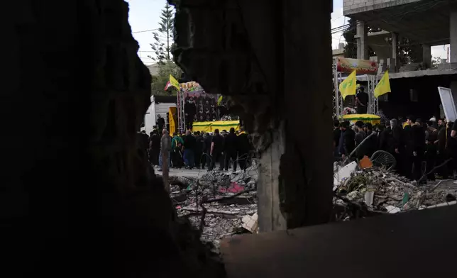 A semi transporting coffins that contain the remains of Hezbollah fighters who were killed before the ceasefire in the war between Hezbollah and Israel, drives past the rubble of a destroyed building, as part of a mass funeral procession in the southern village of Kfar Sir, Lebanon, Tuesday, April 21, 2026. (AP Photo/Hassan Ammar)