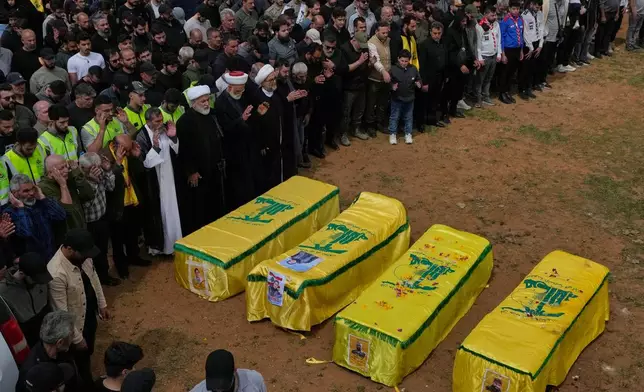 Mourners pray on the coffins of Hezbollah fighters and civilians who were killed in the war between Hezbollah and Israel during a mass funeral in Bazouriyeh village, south Lebanon, Monday, April 20, 2026. (AP Photo/Mohammed Zaatari)