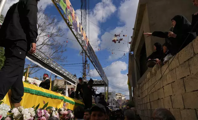 A woman, right, throws flowers over the coffins of Hezbollah fighters, who were killed before the ceasefire in the war between Hezbollah and Israel, during a mass funeral procession in the southern village of Kfar Sir, Lebanon, Tuesday, April 21, 2026. (AP Photo/Hassan Ammar)