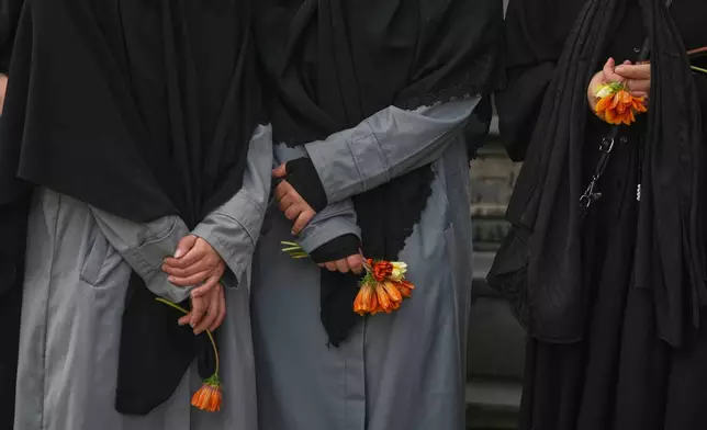 Women hold flowers during a mass funeral procession for Hezbollah fighters killed before the ceasefire in the war with Israel in the southern village of Kfar Sir, Lebanon, Tuesday, April 21, 2026. (AP Photo/Hassan Ammar)
