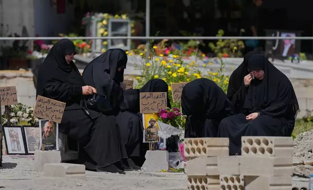 Relatives of a Hezbollah fighter mourn on his grave at a cemetery where civilians and Hezbollah fighters killed in Israeli airstrikes are temporarily buried in the southern port city of Sidon, Lebanon, Tuesday, April 14, 2026. (AP Photo/Mohammed Zaatari)