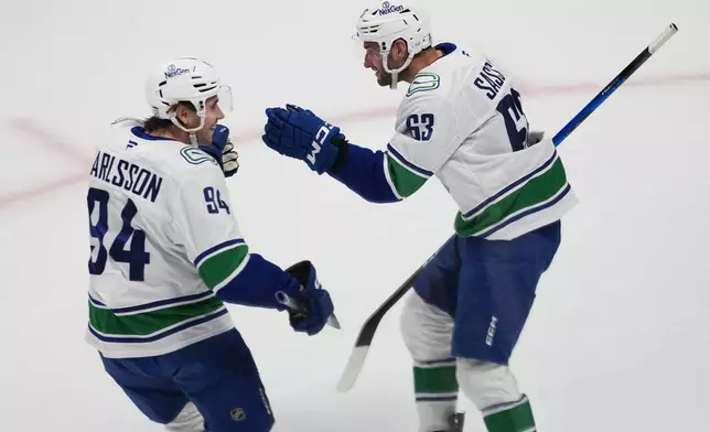 Vancouver Canucks center Linus Karlsson, left, congratulates center Max Sasson after his goal against the Colorado Avalanche in the first period of an NHL hockey game Wednesday, April 1, 2026, in Denver. (AP Photo/David Zalubowski)