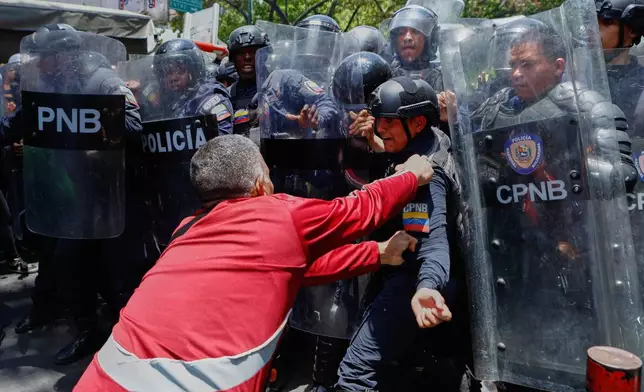 A protester grabs a Bolivarian National Police officer as police try to stop protesters who are demanding higher salaries, pensions and benefits, from continuing their march to the Miraflores Presidential Palace in Caracas, Venezuela, Thursday, April 9, 2026. (AP Photo/Pedro Mattey)