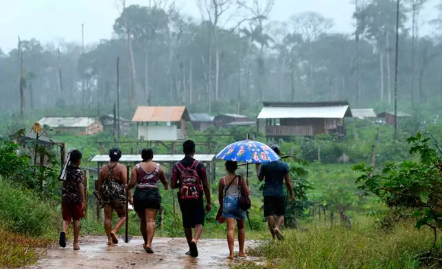 A family walks carrying tools toward an area known as Nova Conquista or New Conquest where families are building houses near the center of Oiapoque, Amapa state, Brazil, Tuesday, March 10, 2026. (AP Photo/Eraldo Peres)