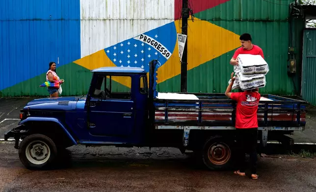 Workers load a vehicle with supplies in front of a wall with an image of the French and Brazilian flags, representing the commercial relationship established along the Oiapoque River between French Guiana and the city of Oiapoque, Amapa state, Brazil, Wednesday, March 11, 2026. (AP Photo/Eraldo Peres)