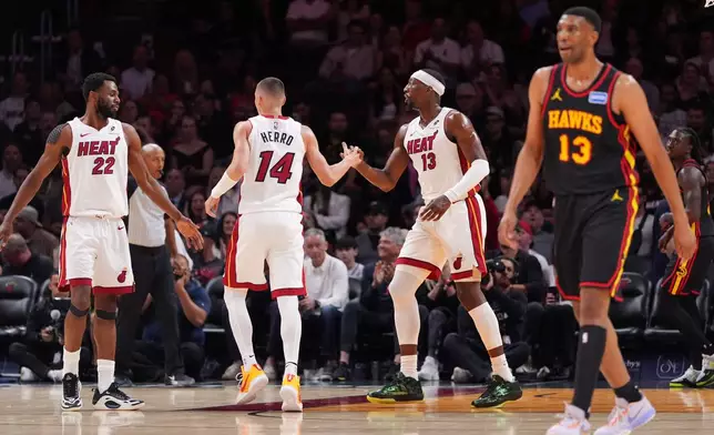 Miami Heat center Bam Adebayo, center right, celebrates with guard Tyler Herro (14) and forward Andrew Wiggins (22) as Atlanta Hawks center Tony Bradley, right, walks downcourt during the first half of an NBA basketball game, Sunday, April 12, 2026, in Miami. (AP Photo/Rebecca Blackwell)