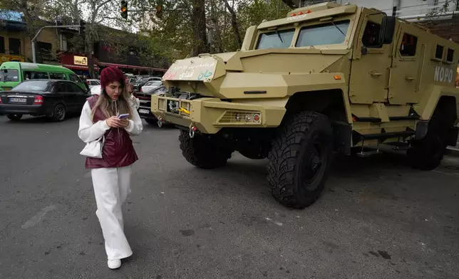 A woman checks her smartphone while walking past a police special forces car at Tajrish Square in northern Tehran, Iran, Sunday, April 12, 2026. (AP Photo/Vahid Salemi)