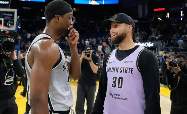 Injured Golden State Warriors guard Stephen Curry, right, talks with San Antonio Spurs forward Harrison Barnes after an NBA basketball game in San Francisco, Wednesday, April 1, 2026. (AP Photo/Tony Avelar)