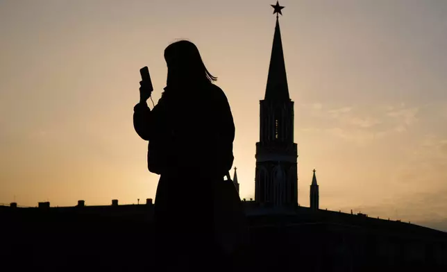 FILE - A woman checks her phone as she walks through Red Square at sunset, in Moscow, Tuesday, March 31, 2026. (AP Photo/Pavel Bednyakov, File)