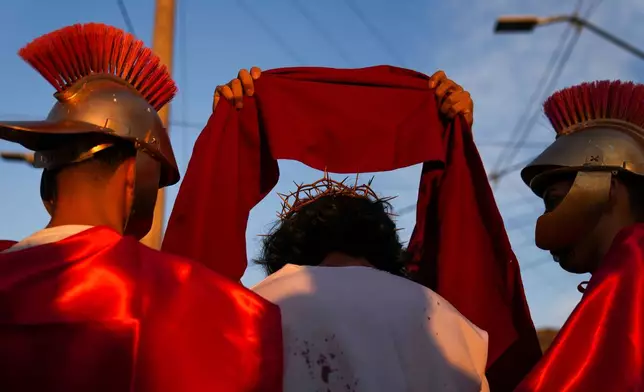 Roman soldiers dress David Sanchez, playing the role of Jesus Christ, with a crown and scarlet cloak to mock his claim as "King of the Jews", during a Way of the Cross reenactment as part of Holy Week celebrations, in Colina, Chile, on Good Friday, April 3, 2026. (AP Photo/Esteban Felix)
