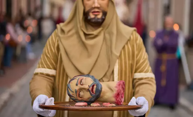 A penitent holds a tray with a figure's severed head, ears, and tongue depicting a biblical scene during a Holy Week procession of the "Hermandad de Nuestro Padre Jesus Nazareno" brotherhood in Puente Genil, southern Spain, Friday, April 3, 2026. (AP Photo/Manu Fernandez)