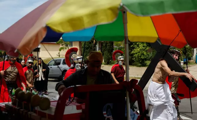 Members of the Resurrection Church walk by a street vendor as they perform during The Stations of the Cross procession through the Boyle Heights neighborhood on Good Friday, April 3, 2026, in Los Angeles. (AP Photo/Caroline Brehman)