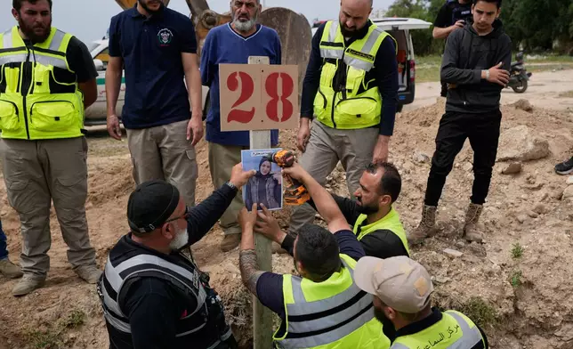 Paramedics attach a portrait over the grave of Ghadir Baalbaki, 19, who was killed on Tuesday in an Israeli airstrike, at a temporary mass grave in the southern port city of Tyre, Lebanon, Wednesday, April 15, 2026. (AP Photo/Hussein Malla)