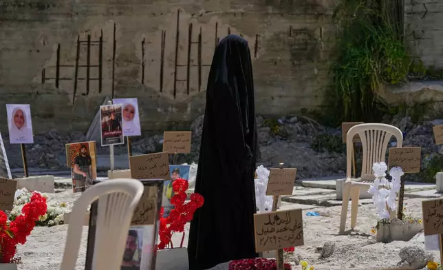 A veiled woman walks through a mass grave where civilians and Hezbollah fighters killed by Israeli airstrikes are temporarily buried in the southern port city of Sidon, Lebanon, Tuesday, April 14, 2026. (AP Photo/Mohammed Zaatari)