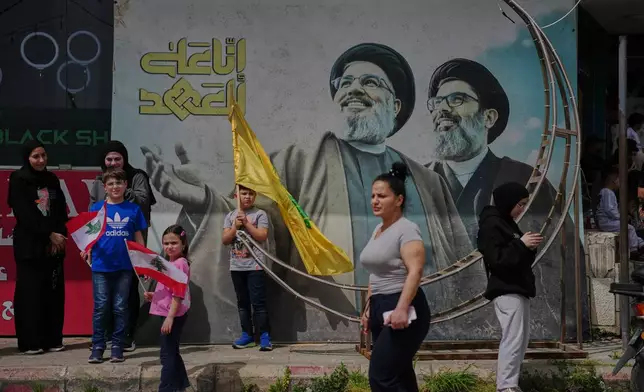 People stand next to a mural with the images of late Hezbollah leaders Hassan Nasrallah, left, and Hashem Safieddine as displaced residents return to their villages following a ceasefire between Israel and Hezbollah, in Zefta, southern Lebanon, Friday, April 17, 2026. (AP Photo/Hassan Ammar)