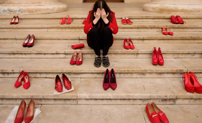A young woman poses for photographers surrounded by pairs of red shoes, a symbol of solidarity with victims of domestic violence, during an awareness event in Bucharest, Romania, Tuesday, March 31, 2026, where organisers said that one woman dies weekly in Romania due to domestic violence. (AP Photo/Andreea Alexandru)